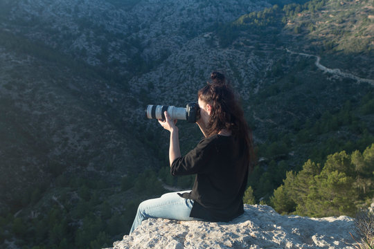 A woman taking photos in the mountains at sunset with a professional photo camera