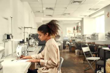 Love To Sew. Young woman seamstress sitting and sewing. Dressmaker working on the sewing machine. Tailor making a garment in her workplace