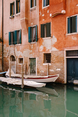 Plakat Boats moored at the walls of a building in a canal in Venice, Italy. Classic Venetian street views - wooden shutters, brick houses, bridges