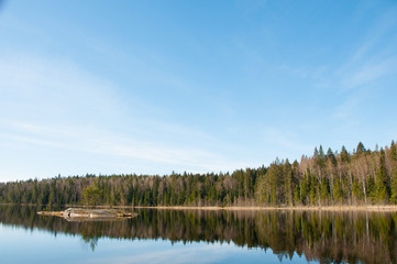 Fototapeta na wymiar Island in the lake. Trees reflected in the calm waters of a forest lake. Wild nature. Natural background. Blue sky over forest and lake. 
