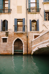Fototapeta na wymiar A brick building in the water in Italy, Venice. A brick bridge over a small narrow canal, classic Venetian windows in the facade of the building with wooden shutters and forged bars.