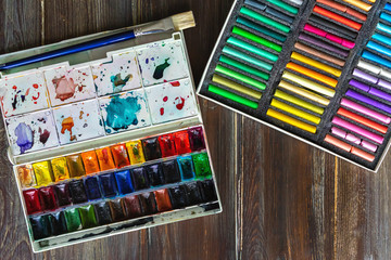 Naklejka premium Flat lay art workplace, wooden table with paint brushes, watercolor paints and crayon pastel chalks. Copy space