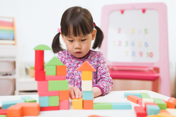 Fototapeta premium toddler girl playing creative toy blocks at home against white background
