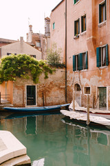Fototapeta na wymiar Boats moored at the walls of a building in a canal in Venice, Italy. Classic Venetian street views - wooden shutters, brick houses, bridges