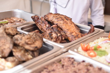 Different food trays of a restaurant, where you see different types of meat including ribs, sausages and rice.