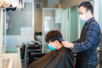 Asian young man and hairdresser man wearing medical mask to protect themselves during novel Coronavirus, Covid-19 in Barbershop Hair Care Service..