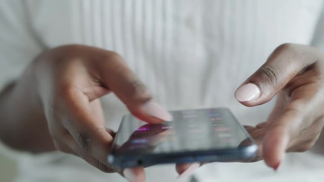 African American woman hands searching for apps on her smartphone, browsing for software application. Frustration for black girl fingers with mobile telephone. Cropped view, close-up