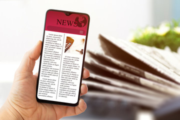 read news on mobile phone and newspapers in the background