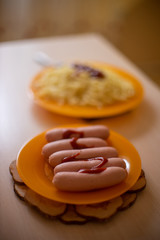 five sausages on an orange plate, on a background a dish with spaghetti