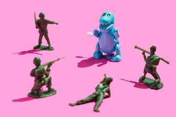 plastic green army men surrounding a tyrannosaurus rex on a pink background