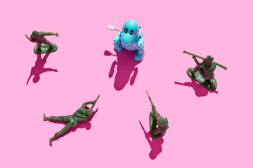 plastic green army men surrounding a tyrannosaurus rex on a pink background