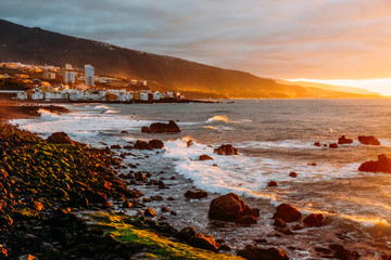 Sunset over the ocean on a tropical island. City in the mountains and ocean at sunset Sunny evening on Tenerife. Pink ocean waves. Background color with gradient and grain, sound effect.
