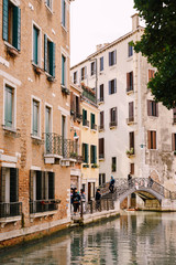 Fototapeta na wymiar Tourists walk on an arable bridge over a small Venetian canal, against the backdrop of apartment buildings on the streets of Venice, Italy.