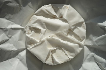 Whole round camembert cheese on a sunny wrapping paper. Top view.