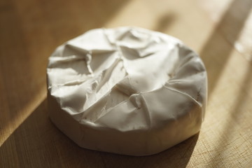 Whole round camembert cheese on a sunny wooden table. Side view, closeup.