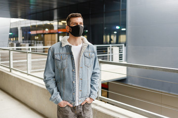 man in a black medical mask stands on an empty city street