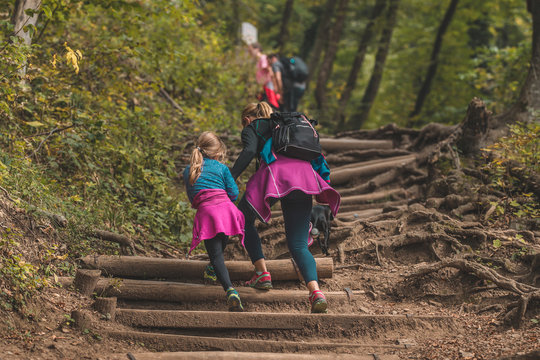 Young woman and a kid with a dog are climbing up the wooden stair path in the mountains on a hiking trip. Young family in sports clothing climbing up on a hill.