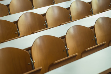 Detail of a multitude of rows of wooden seats in a classroom or in college, with white desk in front of them. Rows of chairs in a classroom.