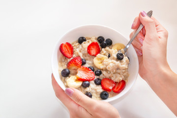 A woman takes a spoonful of oatmeal porridge with strawberries and other fruits
