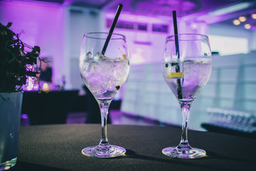 Two gin tonic drinks served on a table next to a green decoration on a party or gala event.