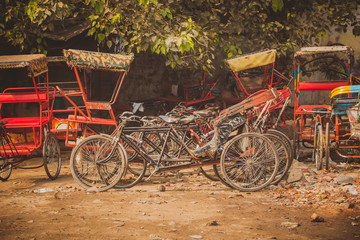 Fototapeta na wymiar Parked bicycle rickshaws in india, multitude of rickshaws in red color and bicycles waiting to be used on a gravel parking lot.