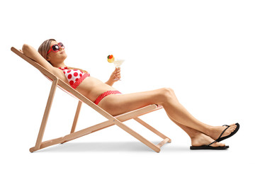 Young woman in bikini sunbathing on a lounge chair and holding a cocktail