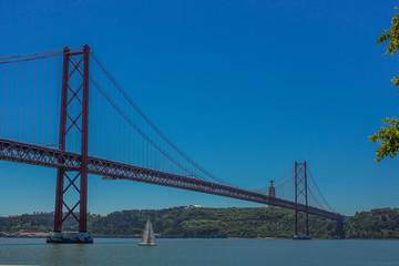 Ponte de 25. april in Lisbon, portugal, taken on a sunny day. A small sailboat is just passing under the bridge.