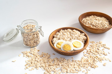 cooked oatmeal porridge in a wooden bowl on a white background with a boiled egg