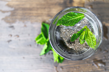 Pure cold water with mint petals and chia seeds on a wooden background. Detox theme. Selective focus.