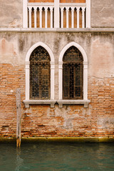 Fototapeta na wymiar The facade of a corporatist apartment building in Venice, Italy. Buildings in waters of Venetian Canal. Typical Venetian windows with arches, columns and a sharp top, on the wall of a stone house. 