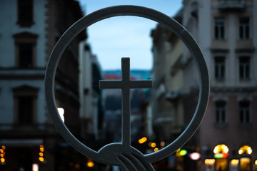 Detail of Christian religious symbol, cross in the foreground with buildings behind.