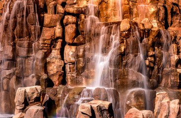 A small waterfall in a park with water flowing down onto brown rocks