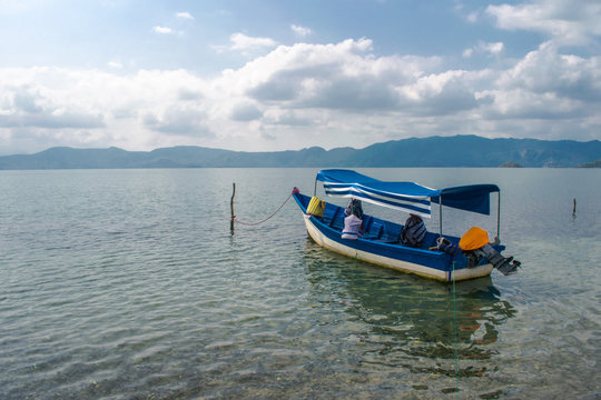 View from the shore of the lake of ilopango a boat inside the crystal clear water of the lake and behind the boat beautiful green mountains. El Salvador