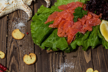 slices of red fish fillet on a wooden background. trout, lettuce, crackers, toasts, red pepper. preparing breakfast
