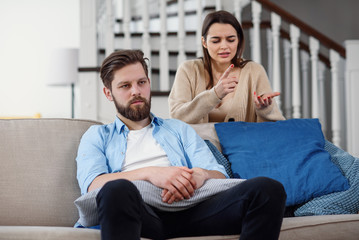 Confused man sits on the couch while his girlfriend yells and quarrels with him at home. Big family...