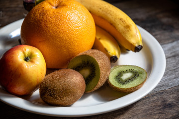 Kiwi, banana, apple, grapefruit in a white plate on the kitchen table. Cooking fruit salad in the home kitchen.