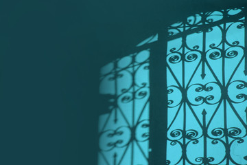 Iron forged grate fence gate contrast shadow on the wall in the morning light. Cool blue cyan...