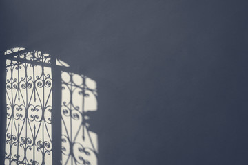 Iron forged grate fence gate contrast shadow on the wall in the morning light. Sad cold blue grey...