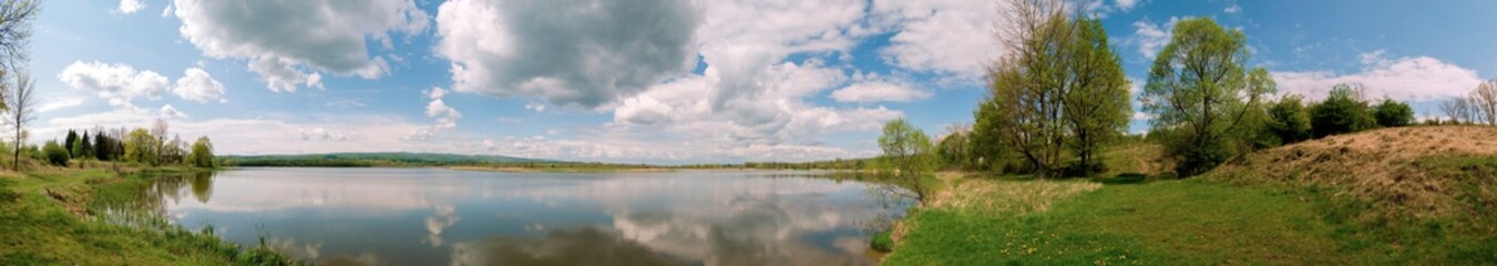 Panoramic landscape from the lake shore with colorful clouds in the spring sun.