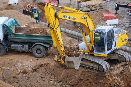 Minsk, Belarus. April 2020. Heavy crawler excavator - New Holland -load sand to the heavy dump truck on construction site. Backhoe at earthworks. Excavator loads dump truck soil dug from the pit