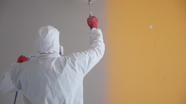 Repair of the apartment. Professional painter paints the walls with white paint spray gun.