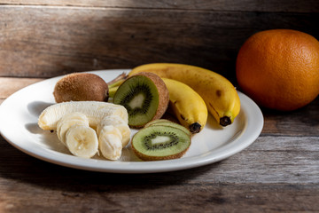 Kiwi, banana, apple, grapefruit in a white plate on the kitchen table. Cooking fruit salad in the home kitchen.