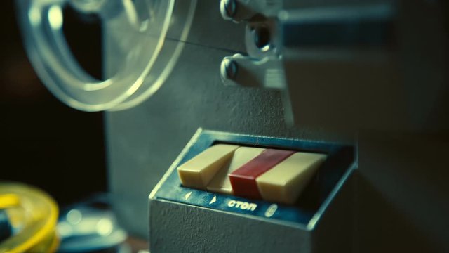 Male hand presses button on old movie projector to test it before watching old movie record, the film reel is starting to rotate, Slow motion.