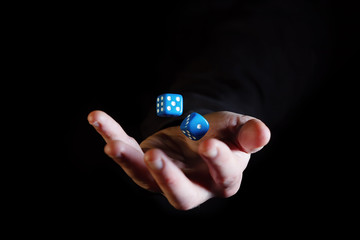 Hand throwing dice cubes in the air against black background