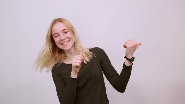Young Blonde Woman In Black Sweater With Stylish Watch On White Background, Happy Attractive Girl Smiling Points Thumbs At The Person behind. Concept Of Guilty People And Charges