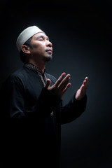 Portrait A good looking middle-aged Asian muslim man is praying for prayer with faith and determination. on black background, with copy space.