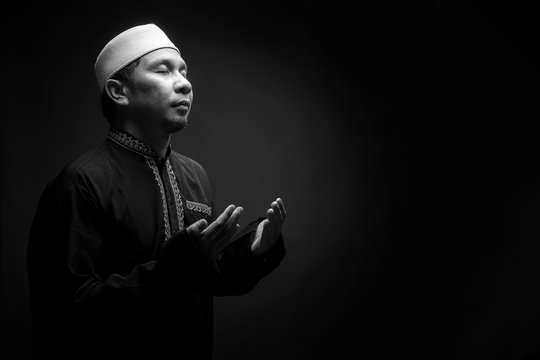 Portrait A good looking middle-aged Asian muslim man is praying for prayer with faith and determination. on black background, with copy space.