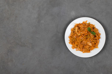 Vegetable dish cabbage stewed with carrots and onions on a plate on a dark gray background top view