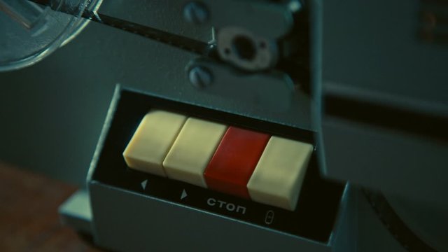 Male hand presses red stop button on retro movie projector to switch the projector off, testing old technology before watching old movie, the film reel stops rotating, light is fading, Slow motion.