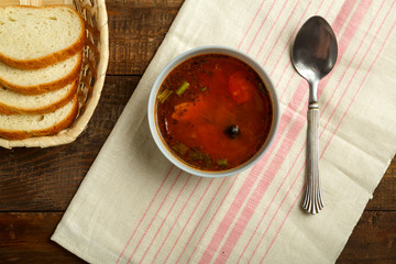 A light cup of Italian tomato soup with potatoes and mushrooms on a wooden table on a napkin and a spoon and bread.